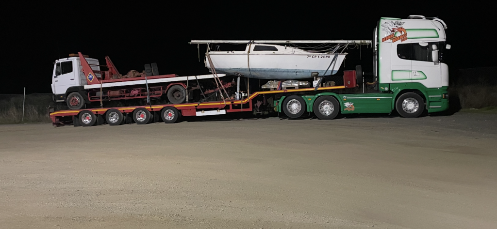 Ein Lastwagen mit einem Boot auf der Ladefläche, beleuchtet von Straßenlaternen in der Nacht.